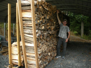 man reaching with arm alongside large stacked firewood pile