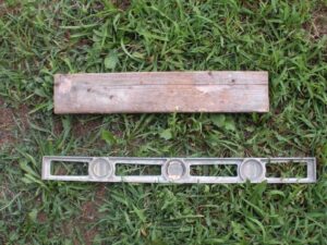 A wooden board and metal ruler laying in the grass.