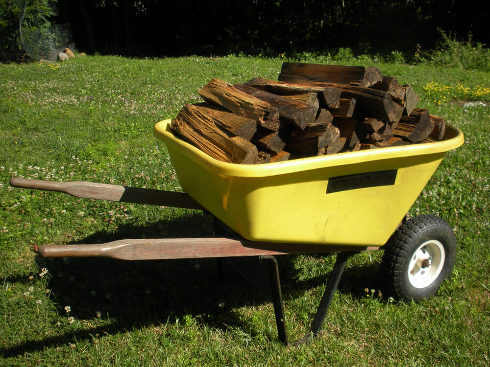 yellow wheel barrow filled with split firewood