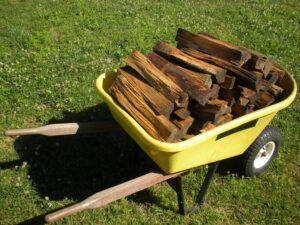 large yellow wheel barrow filled with split firewood