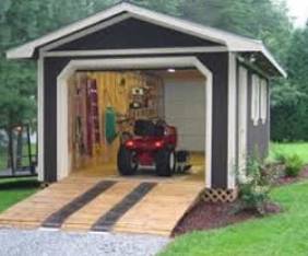 gray with white trim outdoor shed with ramp leading to open door and garden tractor inside