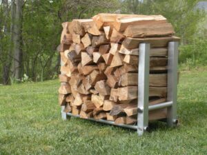 aluminum firewood holder filled with split firewood resting on green grass in backyard with trees in background
