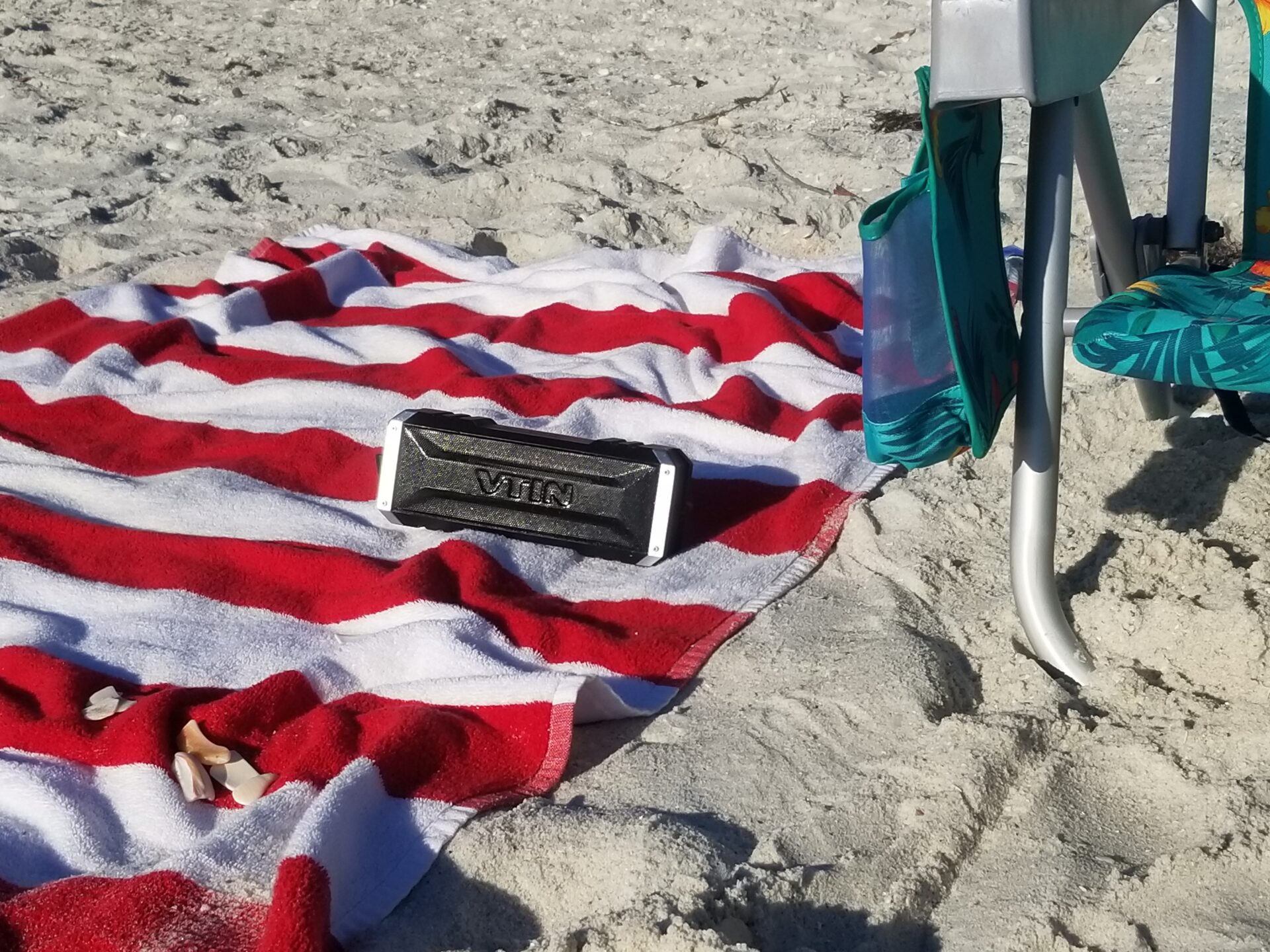 rectangular portable speaker on striped beach towel on sandy beach