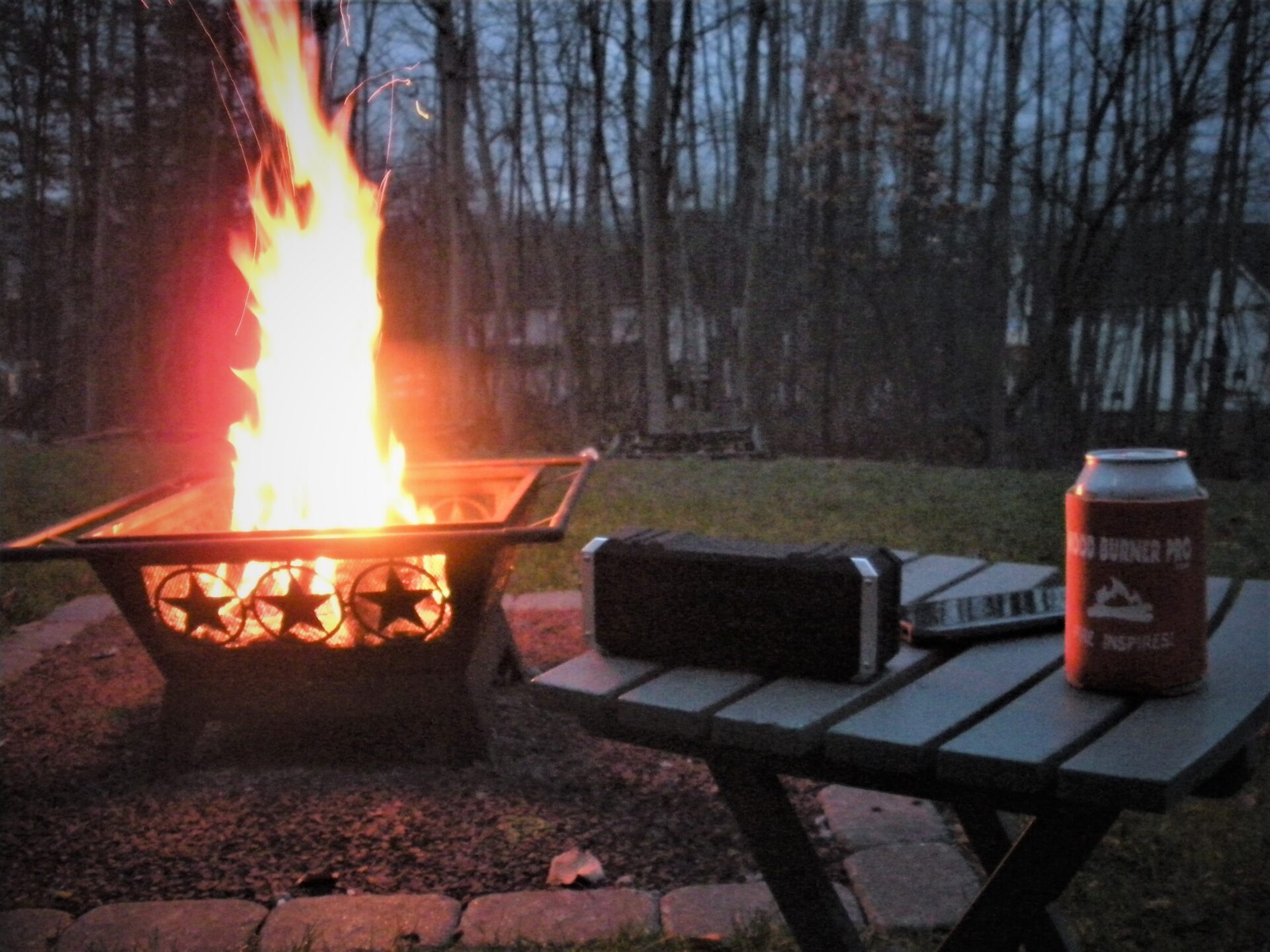 portable speaker, MP3 player and canned beverage on table outdoors by firepit