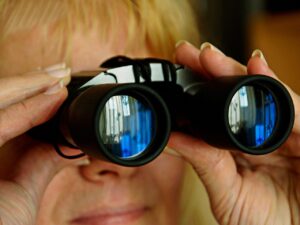 A woman looking through binoculars with her hand on the side of her face.
