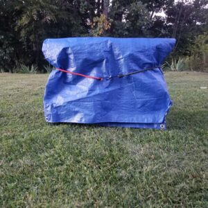 blue tarp covering TFH-1 firewood holder strapped by 2 bungee cords