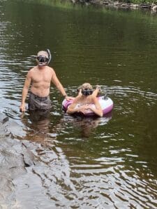 A man and a boy with snorkel masks on wading and floating on a tube in stream