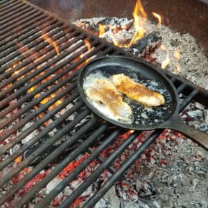 fresh trout sizzling with butter in a cast iron frying pan on a grate over an open fire